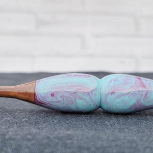 May include: A wooden crochet hook with a blue and pink marbled handle. The hook is made of wood and has a smooth finish.