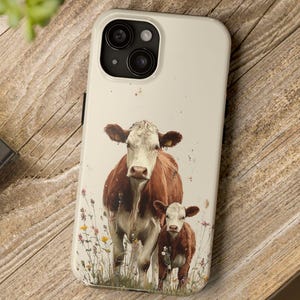 May include: A phone case featuring a watercolor illustration of a cow and calf standing in a field of wildflowers. The case has a cream-colored background and a glossy finish. The cow and calf are brown and white.