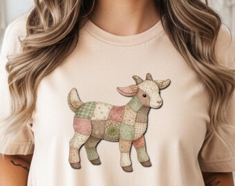 May include: A beige t-shirt featuring a patchwork goat design. The goat is depicted in various pastel colors, including pink, green, and beige. The shirt has short sleeves and a crew neck.