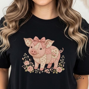 May include: Black t-shirt featuring a charming pig illustration. The pig is adorned with a pink bow and patchwork design, surrounded by floral accents. The design is centered on the front of the shirt.