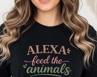 May include: Black t-shirt with the text "ALEXA feed the animals" in a script font. The text is in shades of brown, pink, and green. The shirt is a crew neck and is being worn by a person.