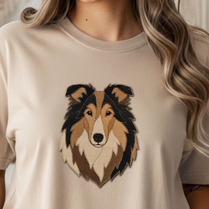 Könnte beinhalten: Beiges T-Shirt mit einem gestickten Porträt eines Collie-Hundes. Der Kopf des Hundes ist mit schwarzem, braunem und beigem Fell dargestellt. Das T-Shirt ist neutralfarben und hat kurze Ärmel.