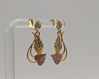 Pode incluir: Um par de brincos de ouro com um design de folhas. As folhas são feitas de três cores diferentes de ouro: amarelo, rosa e verde.