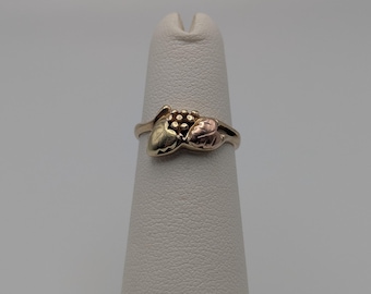 Puede incluir: Anillo de oro con diseño de racimo de uvas y hojas en tres colores. El anillo tiene una banda de oro amarillo, un racimo de uvas de oro amarillo, una hoja de oro rosa y una hoja de oro verde.