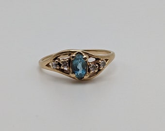 Puede incluir: Un anillo de oro con una piedra preciosa ovalada azul y piedras preciosas más pequeñas transparentes en la banda.