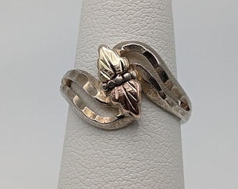 Puede incluir: Un anillo de plata con un diseño de hoja de oro y oro rosa. El anillo está en un expositor blanco.