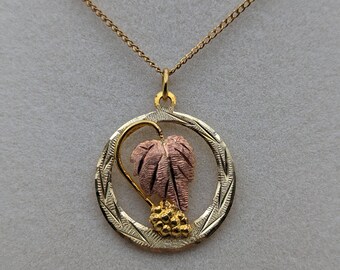 May include: A gold chain necklace with a pendant featuring a pink and gold leaf design inside a circular frame.