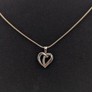 May include: A silver chain necklace with a heart-shaped pendant. The pendant is made of two intertwined hearts with a row of small diamonds in the center.