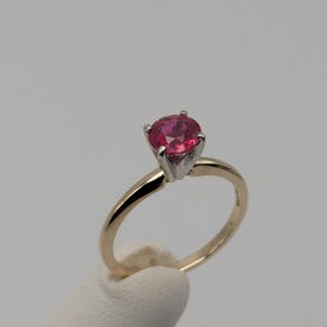 May include: A gold ring with a single round red gemstone set in a prong setting.