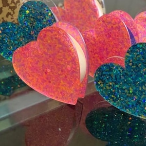 May include: A set of heart-shaped ornaments with glitter. The hearts are pink and blue with a sparkly finish.