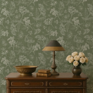 May include: A dark wooden dresser with a decorative floral design holds a lamp, books, a bowl, and a vase of roses. The lamp has a brown and gold shade. The background is a green floral wallpaper.