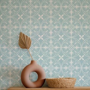 May include: A decorative scene featuring a light blue and white patterned wallpaper background. A brown vase with a circular opening holds a dried palm leaf. A woven basket sits on a wooden surface, creating a natural, neutral aesthetic.