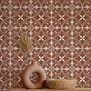 May include: A terracotta-colored vase with a circular opening and a woven basket sit on a wooden surface. The background features a repeating white floral pattern on a terracotta-colored fabric.