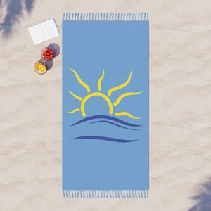 K&ouml;nnte beinhalten: Hellblaues Strandtuch mit gelbem Sonnendesign und blauen Wellen. Das Handtuch hat Fransen an den kurzen Enden. Das Handtuch ist rechteckig und etwa 152 cm lang.