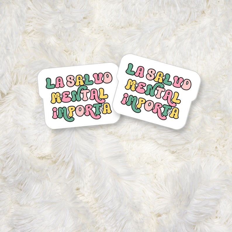 May include: Two white stickers with the text "LA SALUD MENTAL IMPORTA" in a retro font, featuring pink, yellow, and green colors. The stickers are on a fluffy white background.