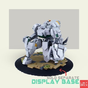 Może przedstawiać: Szara i biała figurka robota zbudowana z zazębiających się klock&oacute;w, ustawiona na czarnej okrągłej podstawie z brązowo-beżową platformą. Robot ma zielone i ż&oacute;łte akcenty. Widoczny jest tekst "DISPLAY BASE".