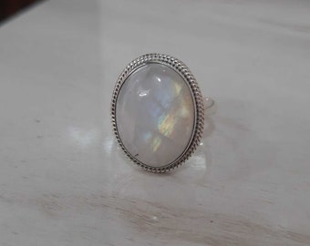 Puede incluir: Un anillo de plata con una gran piedra de luna ovalada engastada en un engaste de cuentas.