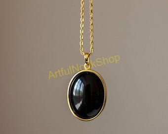 Pode incluir: Um colar de corrente de ouro com um pingente oval preto. O pingente tem uma superfície lisa e brilhante.