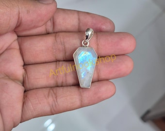 Op de afbeelding: Een doodskistvormige hanger met een zilveren balein. De hanger heeft een grote, iriserende maansteen met blauwe en gele flitsen. De edelsteen is gezet in een zilveren bezel. De hanger wordt in een hand gehouden.