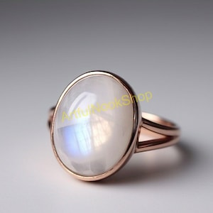 May include: A rose gold ring with a large oval moonstone. The moonstone has a blue iridescent sheen.