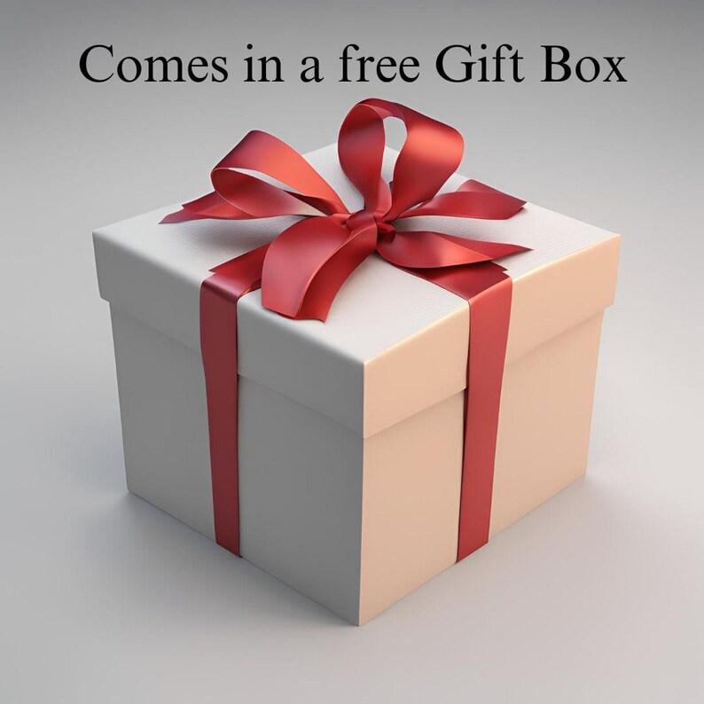 以下が含まれることがあります： 赤いリボンと蝶結びが付いた白いギフトボックス。ボックスは正方形で閉じられています。「Comes in a free Gift Box」というテキストが画像の上部にあります。