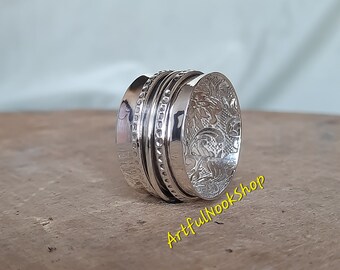 May include: A silver spinning ring with a floral design. The ring is made of multiple bands that spin around each other.