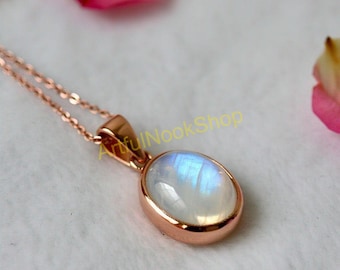 May include: A delicate rose gold chain necklace with a white oval moonstone pendant. The moonstone has a shimmering iridescent effect.