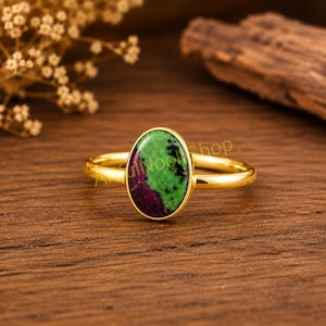 May include: A gold ring featuring an oval-shaped zoisite gemstone with distinct green and deep purple inclusions. The smooth, polished gold band holds the stone in a simple bezel setting, showcasing the natural colour contrast of the mineral.