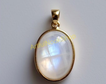 May include: A gold pendant with a large oval-shaped moonstone. The moonstone is iridescent and has a white and blue color.