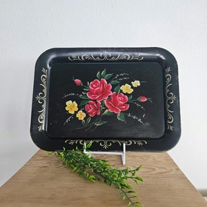 May include: Black metal serving tray with a floral design featuring red roses and yellow flowers. The tray has a gold trim around the edges.