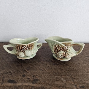 May include: A set of two vintage green and brown ceramic creamer and sugar bowls with a pine cone design.
