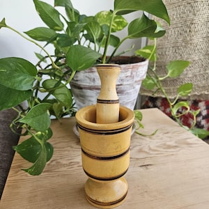 May include: A yellow wooden mortar and pestle with black stripes. The mortar has a wide base and a round bowl. The pestle is cylindrical and fits snugly inside the bowl.