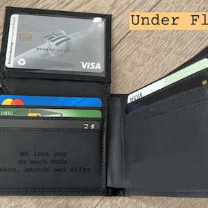 May include: Black leather wallet with multiple card slots, holding various credit and debit cards. The wallet is open, revealing the interior with the text "We love you so much Dady Jason, Amanda and wifey". The text "Under Flap" is also visible.