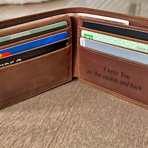 May include: Open brown leather wallet with multiple card slots filled with various credit and debit cards. The interior of the wallet has the engraved text "I love You to the moon and back".