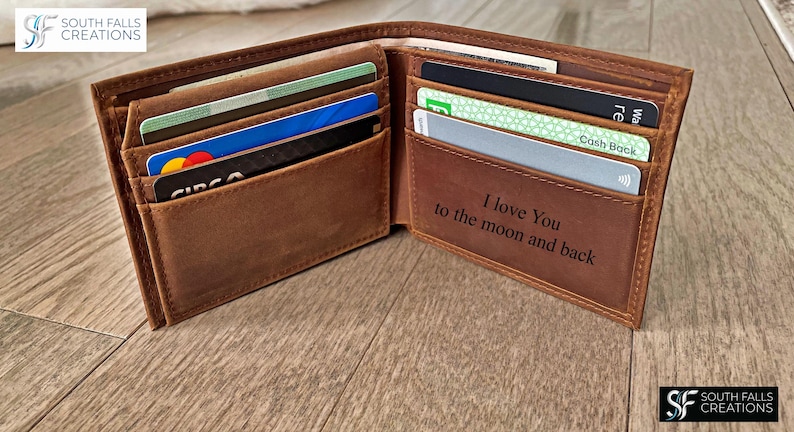 May include: Open brown leather wallet with multiple card slots filled with various credit and debit cards. The interior of the wallet has the engraved text "I love You to the moon and back".