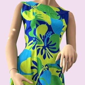 May include: A sleeveless dress featuring a vibrant floral pattern in shades of lime green, bright blue, and dark blue. The garment has a boat neckline and a fitted bodice with vertical seams, showcasing large hibiscus-style flower motifs throughout.