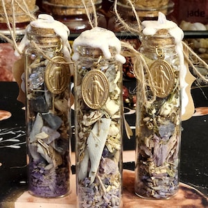 Peut inclure: Trois petites bouteilles en verre remplies d'herbes séchées et de cristaux. Chaque bouteille a un bouchon en liège scellé avec de la cire blanche, un pendentif doré et une boucle en ficelle. Le contenu comprend des plantes séchées violettes et vertes.
