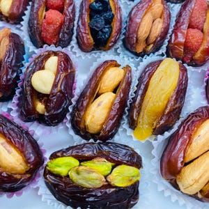 May include: Close-up of assorted dates, each filled with different ingredients. Some dates are filled with almonds, pistachios, dried berries, or other fruits. The dates are arranged in small, decorative paper cups.