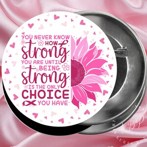May include: A white button with a pink sunflower and pink hearts. The button has the text "You never know how strong you are until being strong is the only choice you have".