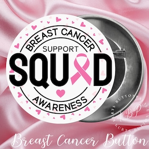 May include: A round button with the words "Breast Cancer Support Squad Awareness" in black text. A pink ribbon and hearts are featured on a white background. The button is set against a pink satin background.