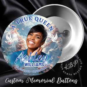 May include: A memorial button with a photo of a woman smiling. The button has a blue background with clouds and doves. The text "A True Queen" is at the top of the button. The text "Ashley Williams" is in the center of the button. The text "04/28/2002 - 01/08/XXXX" is at the bottom of the button.