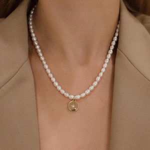May include: A delicate pearl necklace with a gold pendant. The pendant is a small, round shape with a starburst design and a small gemstone. The pearls are white and oval-shaped, strung together to form a necklace.