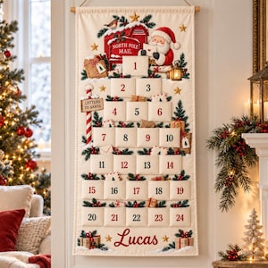 Può includere: Un calendario dell'avvento in tessuto color crema da appendere alla parete con una cassetta postale rossa North Pole Mail, Babbo Natale e tasche numerate da 1 a 24. Il design include rami di pino verdi, bacche rosse, stelle dorate e il nome Lucas.