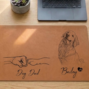 May include: A rectangular brown desk mat with a dog-themed design. The mat features a line drawing of a dog's paw bumping a fist, the words "Dog Dad", a dog portrait, the name "Bailey", and a heart with a paw print.