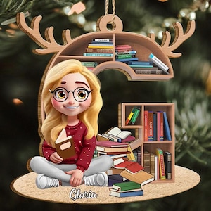 May include: A wooden Christmas ornament depicting a cartoon girl with blonde hair, glasses, and a red sweater, holding a book. The ornament has a bookshelf design with books and the name "Gloria".