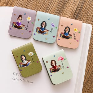 Può includere: Cinque segnalibri magnetici colorati con illustrazioni di ragazze che leggono libri. Ogni segnalibro presenta una ragazza, un fiore e un nome diversi. I segnalibri sono in tonalità di viola, blu, pesca, verde e verde chiaro. Farfalle sparse.