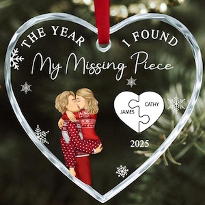 May include: Clear heart-shaped glass Christmas ornament with a red ribbon. The ornament has the text "THE YEAR I FOUND My Missing Piece" and a couple embracing. Includes names "JAMES" and "CATHY" and the year "2025".