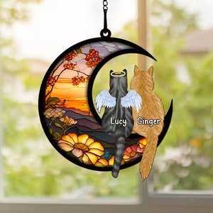 Puede incluir: Un carillón de viento de vidrio tintado en forma de luna con dos gatos sentados en él. El gato de la izquierda tiene un halo y alas y se llama "Lucy". El gato de la derecha se llama "Ginger". El fondo es una escena de puesta de sol con flores.