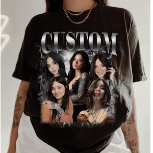 Può includere: Maglietta nera con la parola "CUSTOM" stampata in lettere argentate. La maglietta presenta un collage di quattro donne con tatuaggi, ognuna con un diverso stile di capelli e un'espressione diversa.