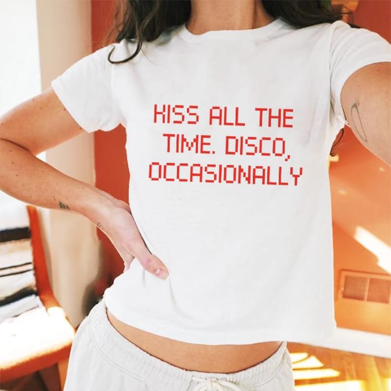 May include: White crop top with the red text "KISS ALL THE TIME. DISCO, OCCASIONALLY." The shirt has short sleeves and a crew neck. The fabric appears to be a soft cotton blend.